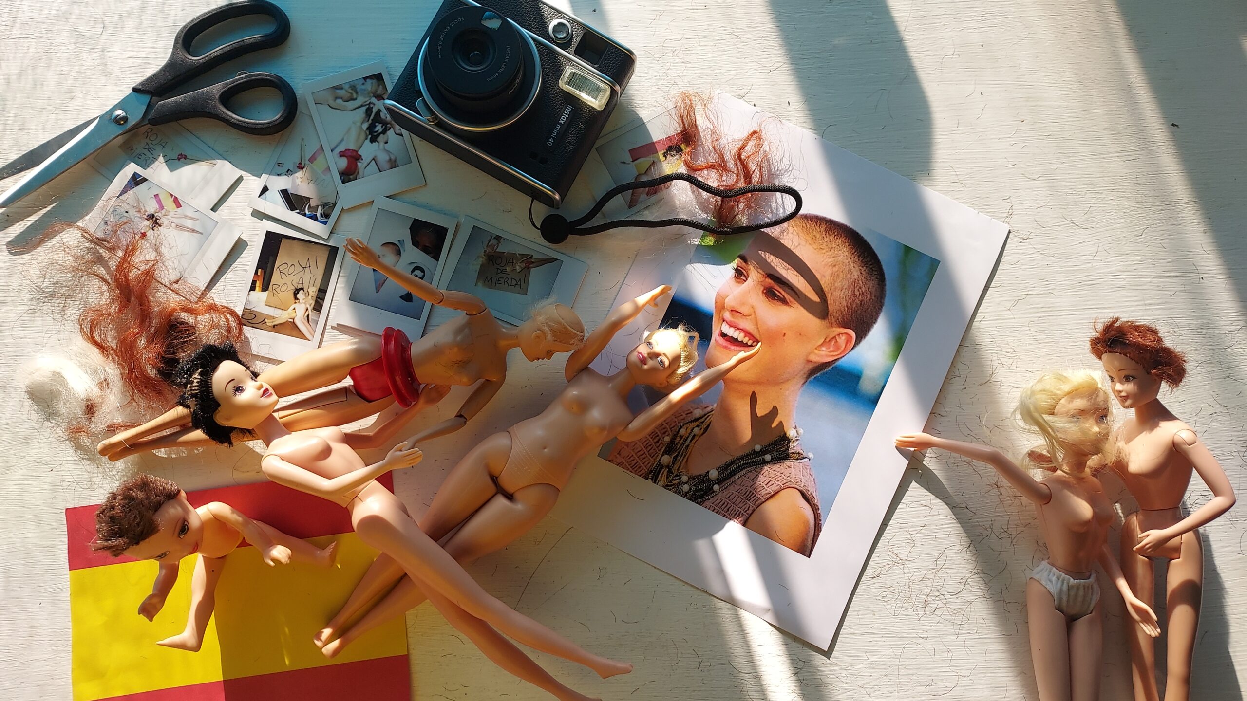varios objetos sobre una mesa, tijeras, fotos, muñecas y bandera de españa